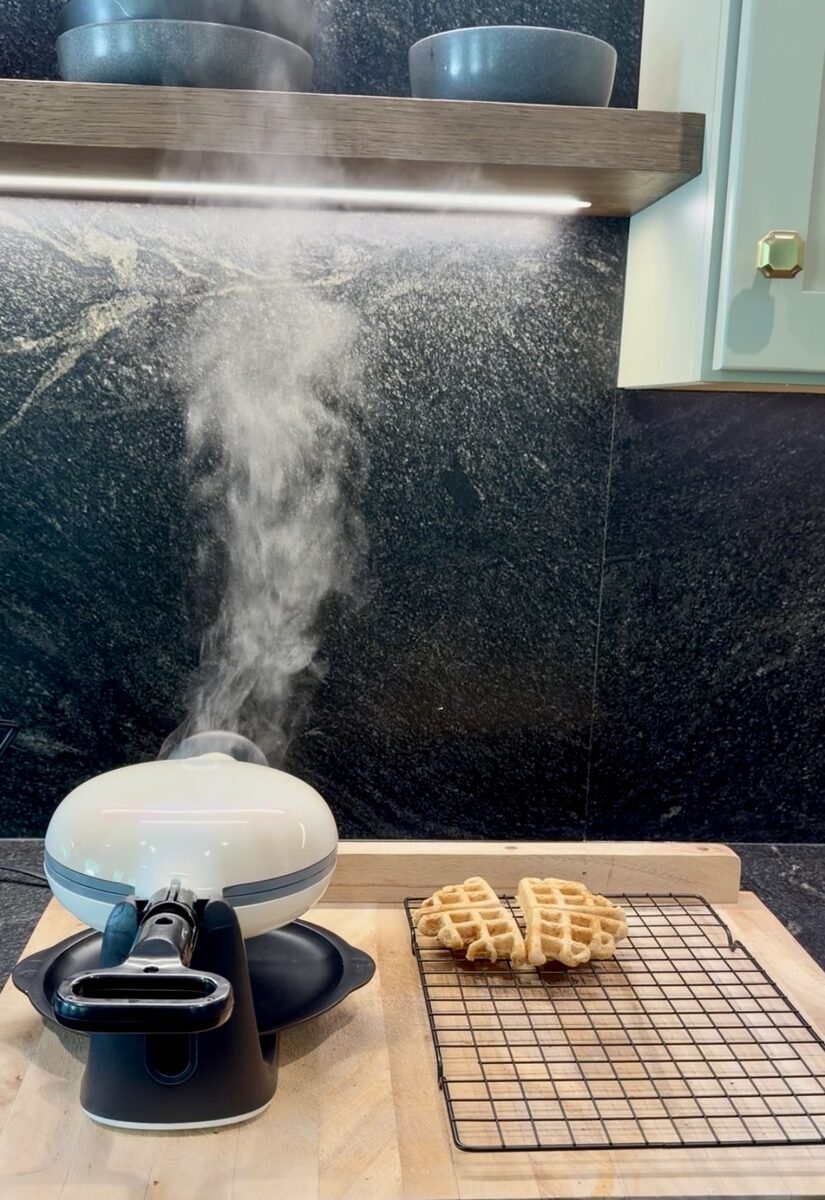 Steam rising from the waffle iron, fresh waffles cooling on a rack